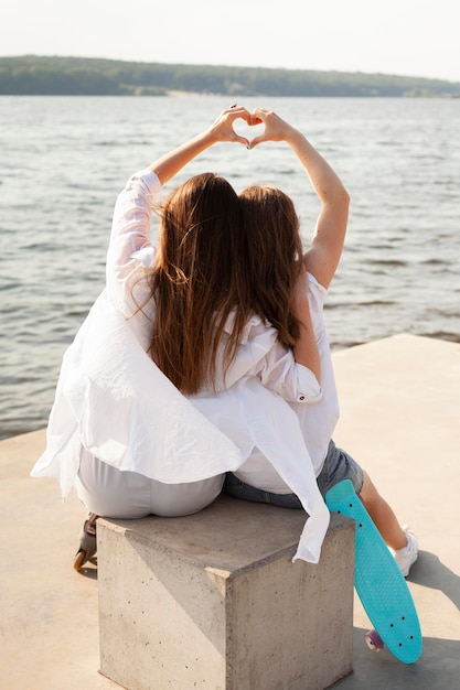 Back view of two women making the love sign by the lake