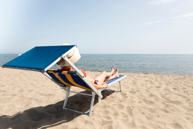 Free Photo back view woman on beach chair sunbathing