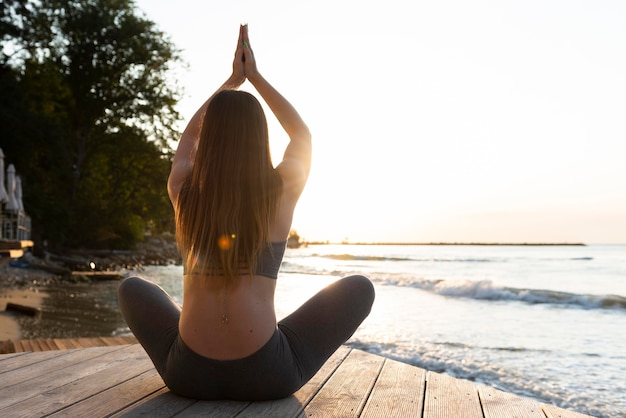 Free photo back view woman doing yoga on the beach