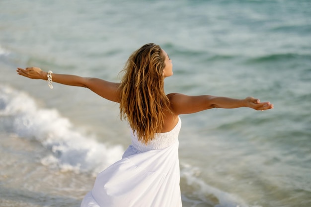 Back view of woman feeling free while standing by the sea with her arms outstretched