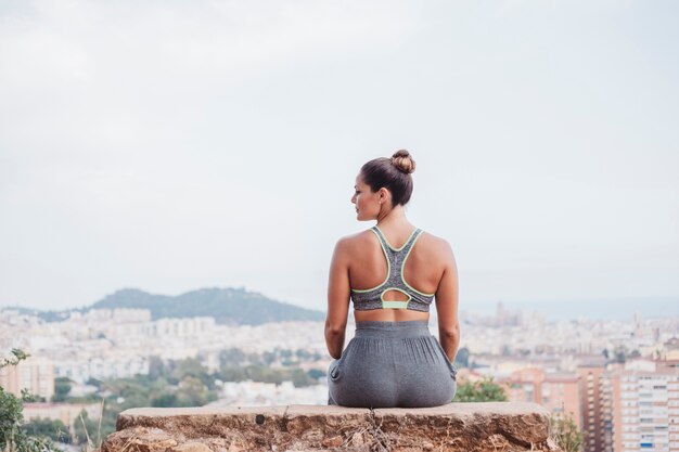 Back view of woman sitting on rock in front of city