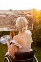 Free photo back view of woman in wheelchair painting outdoors