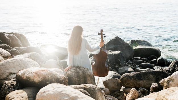 Back view of woman with cello by the ocean