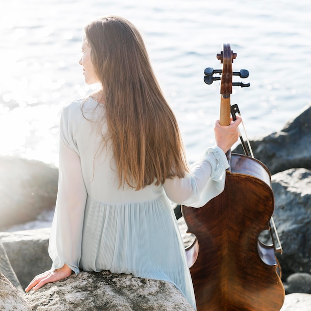 Free photo back view of woman with cello by the sea