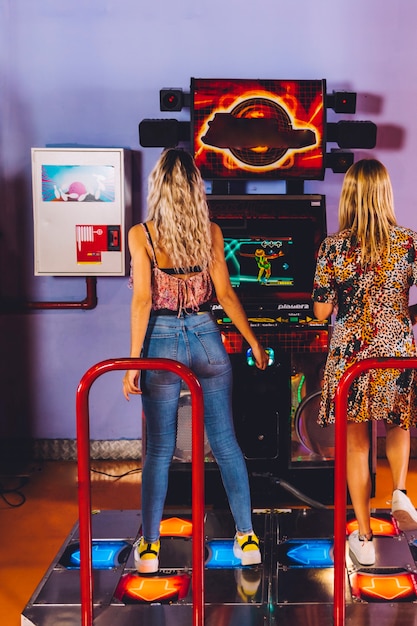 Back view women playing dancing arcade