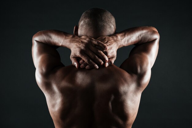 Back view of young african man with muscular body holding his neck