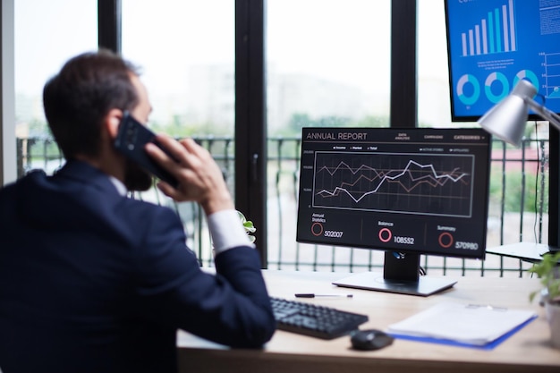 Back view of young entrepreneur talking on the phone with his business partner. Digital graphics on computer monitor.