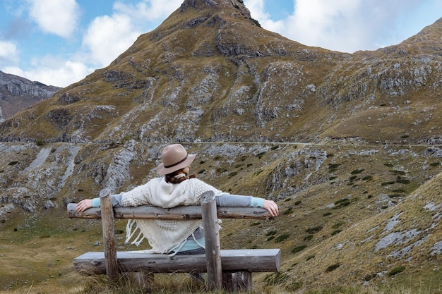 Back view of young lady with hat and warm poncho on mountain landscape Durmitor Montenegro