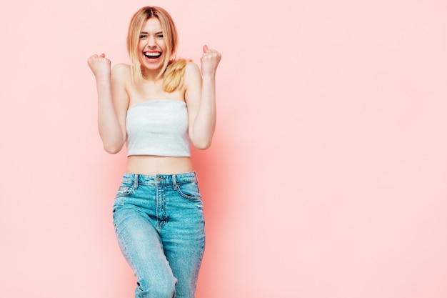 Free photo back of young beautiful smiling blond female in trendy summer clothes sexy carefree woman posing near pink wall in studio positive model having fun indoors cheerful and happy