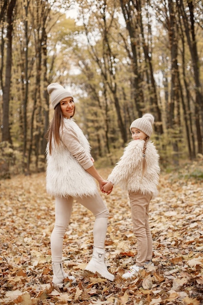 Free Photo backside photo of a woman with little girl walking in autumn forest. brunette woman play with her daughter. girl wearing beige sweater and mother wearing white clothes.