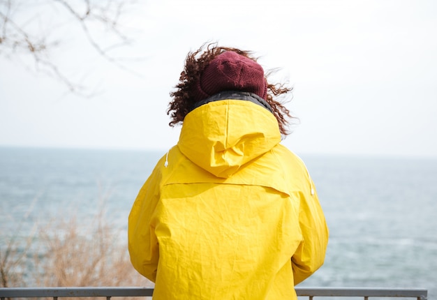 Free Photo backview shot of woman looking away at sea in yellow raincoat