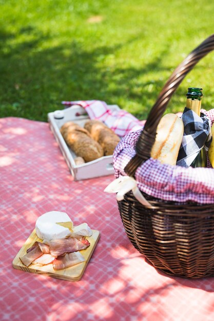 Bacon and cheese on chopping board over the cloth with picnic basket