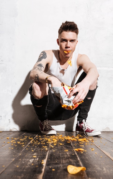 Free Photo bad man with tattoo eating potato chips from the packet