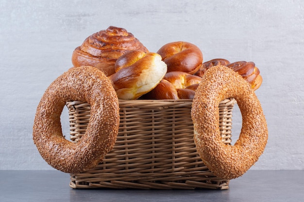 Bagels hanging from a basket full of sweet buns on marble background. High quality photo