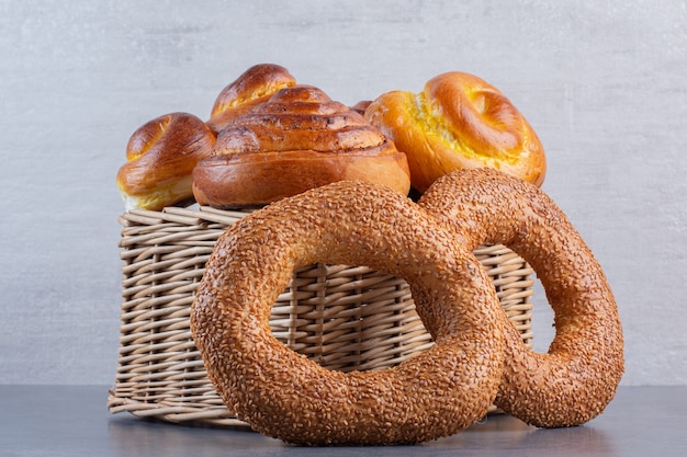 Bagels leaning against a basket full of sweet buns on marble.