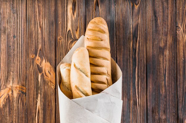 Baguettes wrapped in the paper over the wooden background