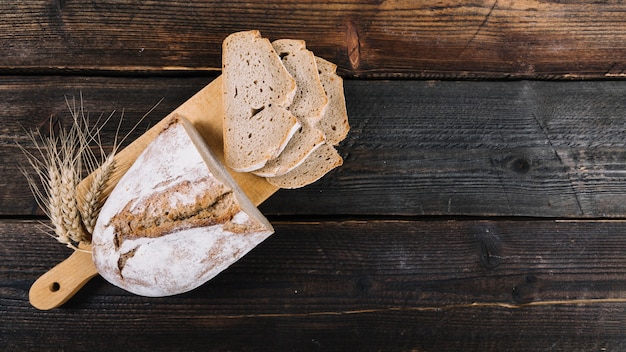 Baked bread and ear of wheat on chopping board over the wooden table