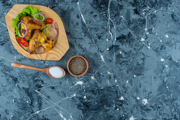 Baked chicken wings and vegetables on a wooden plate , on the blue background. 