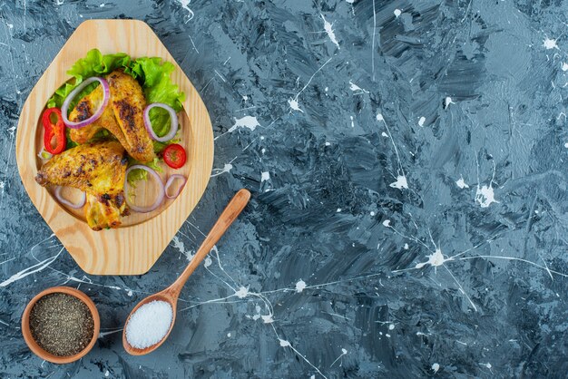 Baked chicken wings and vegetables on a wooden plate, on the blue background.