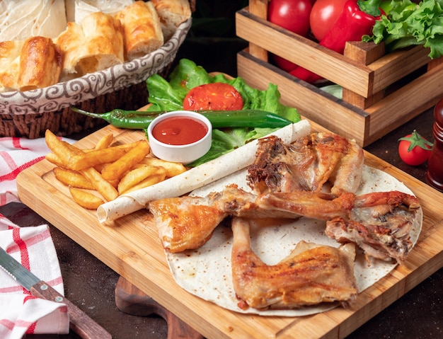 Baked chicken wings with French fries in lavash with vegetables and ketchup on wooden board