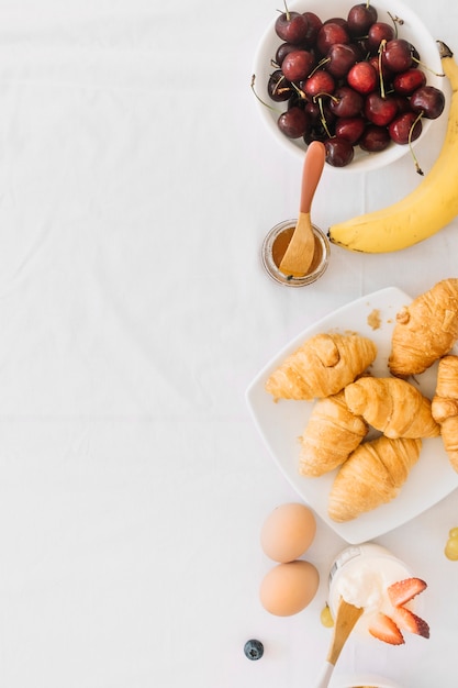 Free photo baked croissant with fruits; egg and yogurt on white backdrop