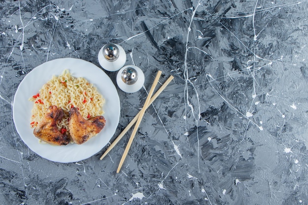 Baked meat and noodle on a plate next to salt and chopstick, on the marble background. 