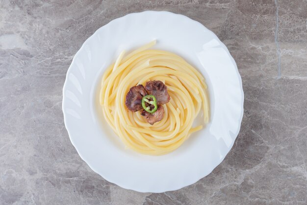 Baked meat over pasta on the plate , on the marble surface.