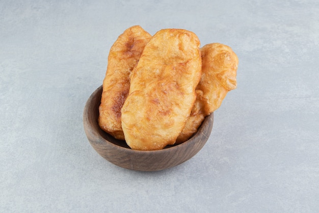 Baked piroshki with potatoes in wooden bowl.