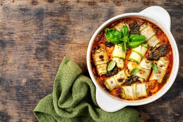 Baked zucchini rolls with ricotta and cheese in marinara sauce on a wooden background Italian style