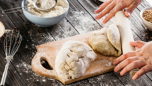 Baker flattening the dough with rolling pin on chopping board