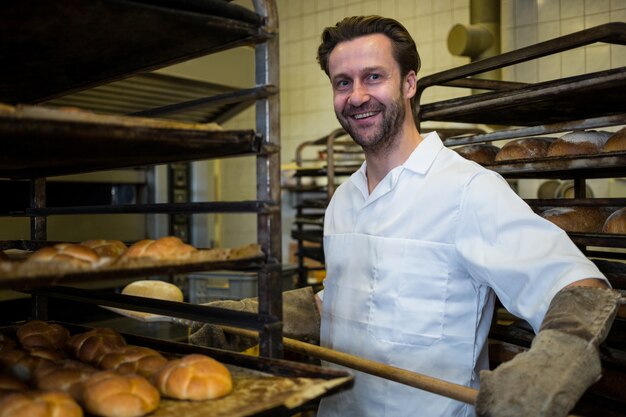 Baker keeping tray of baked buns in shelf