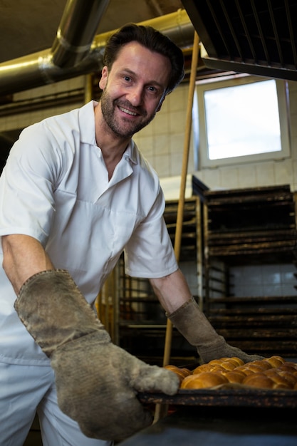 Baker keeping tray of baked buns in shelf