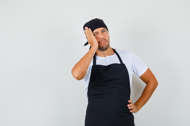 Baker man looking up in t-shirt, apron and looking pensive.