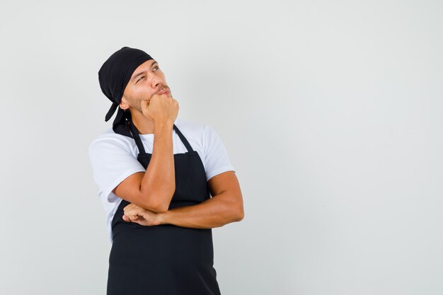 Baker man looking up in t-shirt, apron and looking pensive