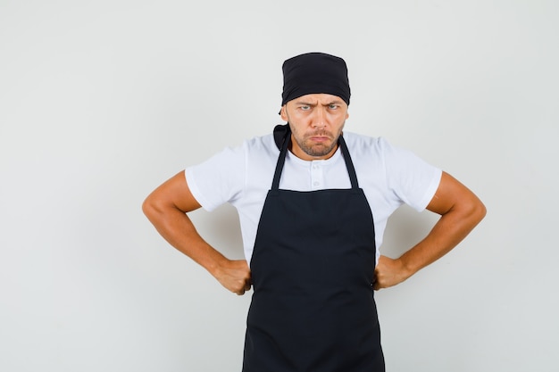 Free photo baker man standing with hands on waist in t-shirt, apron and looking rageful