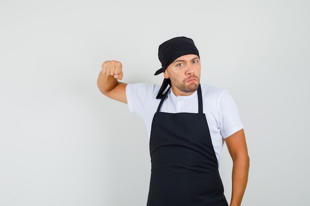 Free photo baker man threatening with fist in t-shirt, apron and looking furious