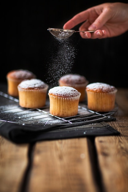 Baker pouring powdered sugar over muffins