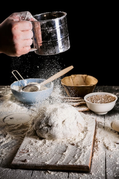 Baker sifting flour through a sieve on wooden table