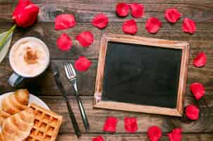 Free photo bakery on plate near cup of drink, flower, cutlery, petals and photo frame