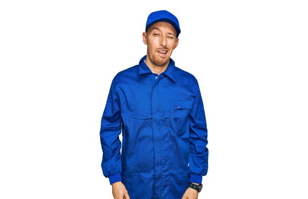 Bald man with beard wearing builder jumpsuit uniform winking looking at the camera with sexy expression cheerful and happy face