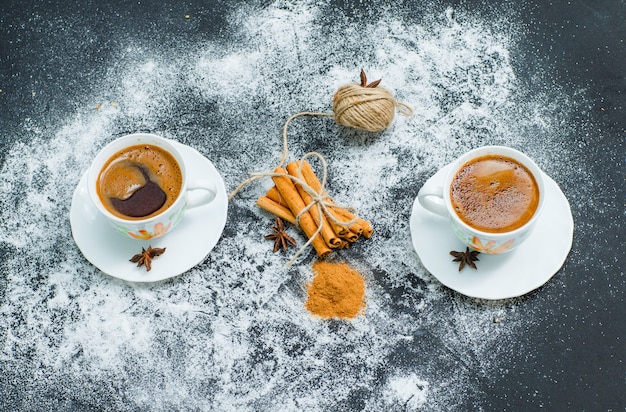 A ball of rope tied to dry cinnamon with cinnamon powder and two cups of coffee high angle view on gray textured surface