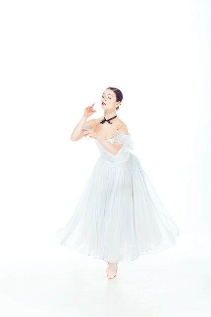 Ballerina in white dress posing on pointe shoes, studio.