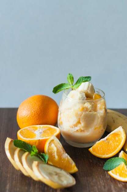 Banana; whole orange; mint and ice cream in glass on wooden table against blue background