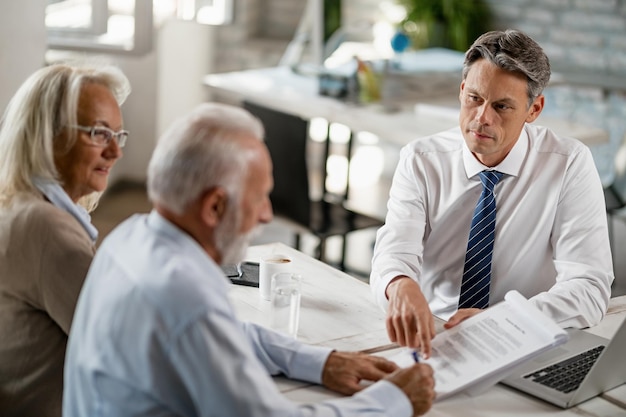 Bank manager having a meeting with senior couple and pointing at place they need to sign on the contract