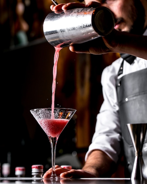 Bar tender pours cocktail from cocktail shaker into martini glass