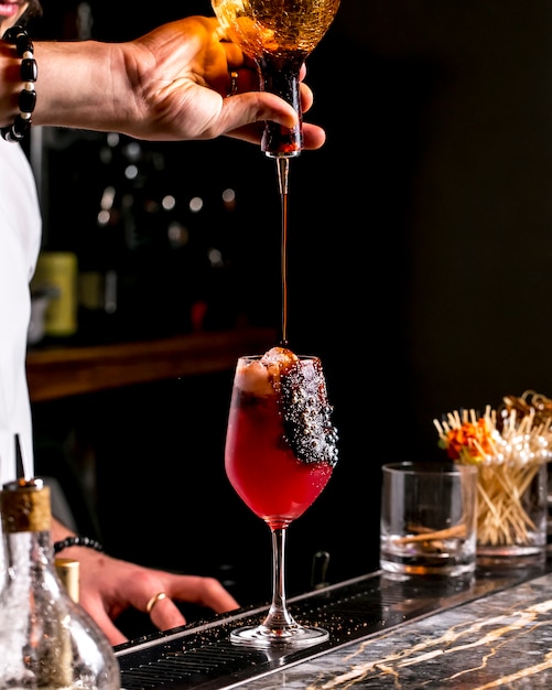 Bar tender pours syrup into red cocktail glass