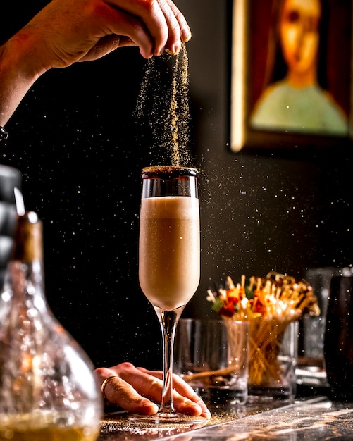 Bar tender sprinkles golden glitter into cocktail in champagne glass