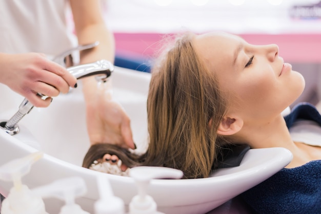 Barber girl combing her hair in beauty saloon. Beautiful lady having her hair washed by hairdresser in hairdressing saloon.