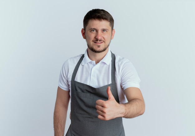 Barber man in apron looking at camera smiling confident showing thumbs up standing over white background