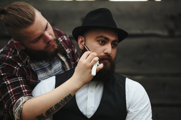 Barber shaves a bearded man in vintage atmosphere